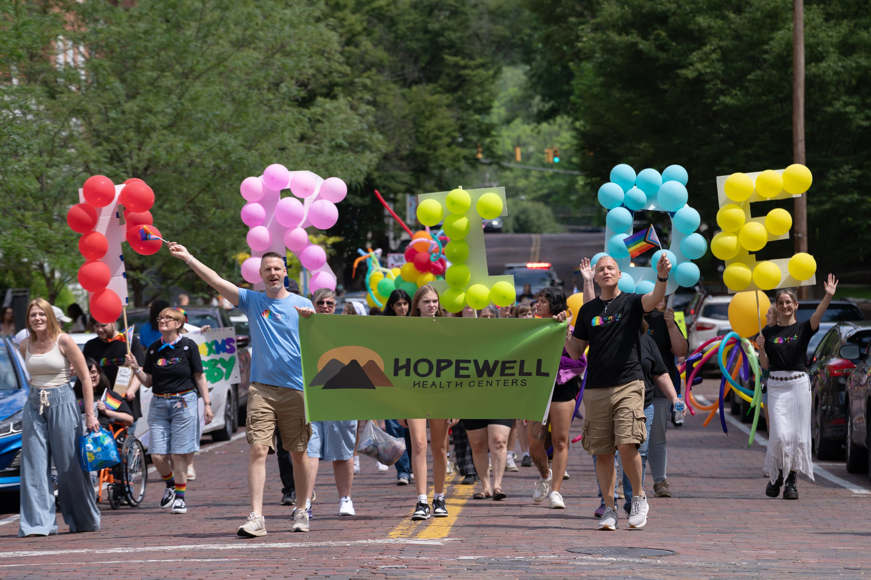 Marchers carry giant balloon letters spelling PRIDE behind a Hopewell Health Centers banner.